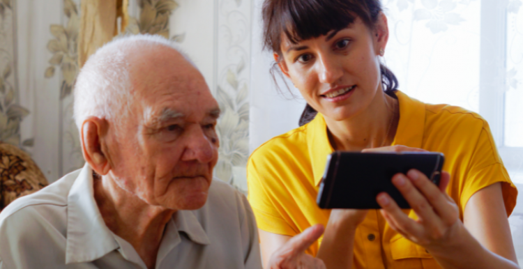 Young woman helping an elderly gentleman work a mobile phone