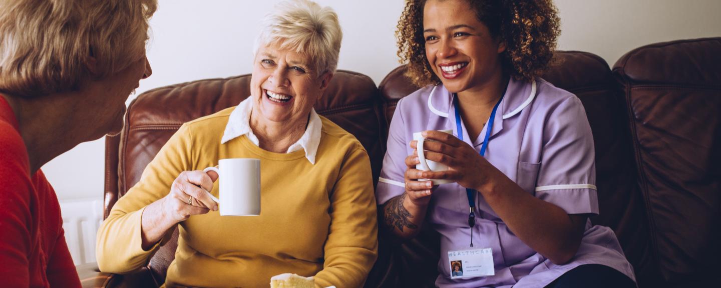 two old women in a care home laughing with their nurse