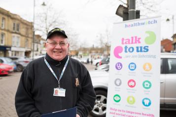 male volunteer standing with Healthwatch banner