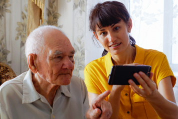 Young woman helping an elderly gentleman work a mobile phone