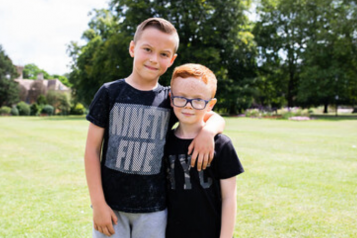 Two young boys facing forward with an arm around shoulders