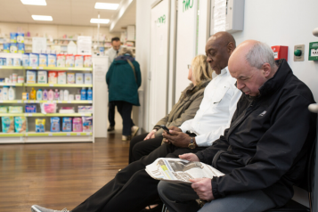 Three people sitting waiting at a pharmacy
