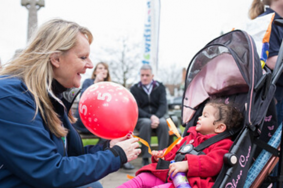 Healthwatch volunteer passing a balloon to toddler in push chair