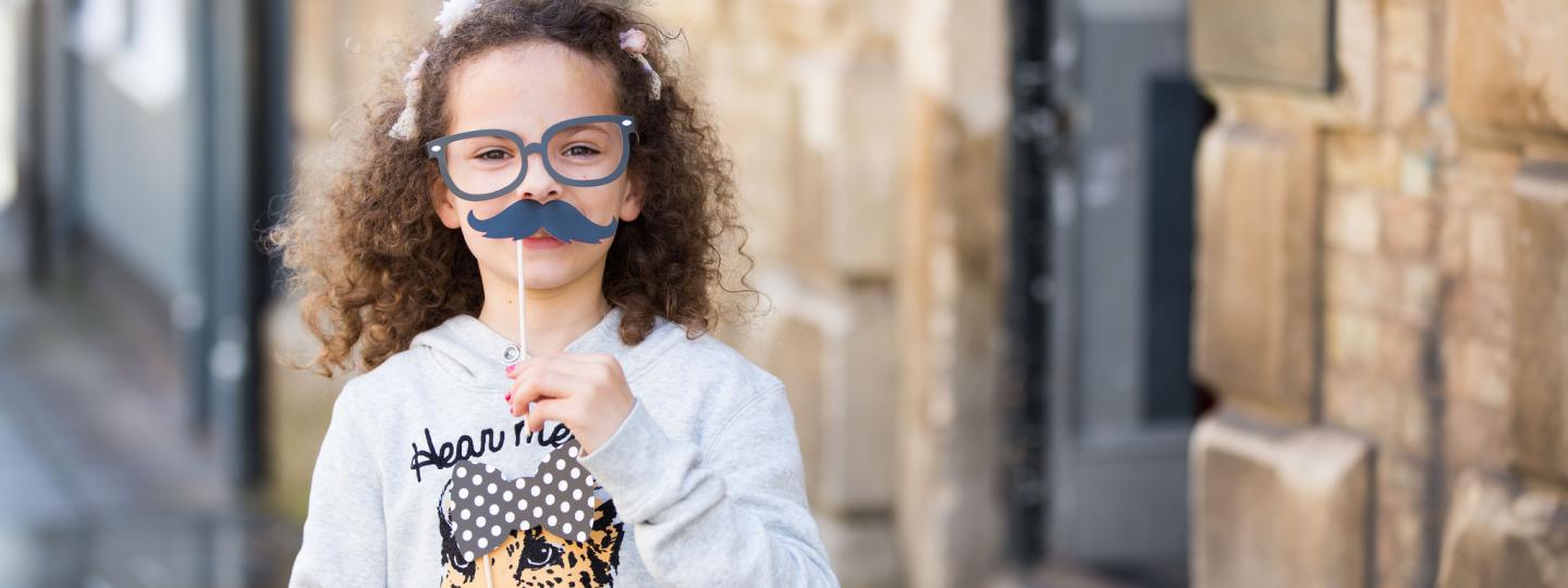 Small child holding up mustache prop for a photograph