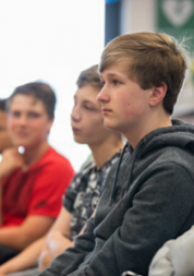 Teenage boy by sitting in a row of teenagers looking towards the front of the room